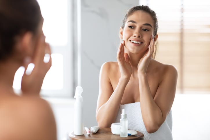 Happy Woman Touching Face Caring For Skin Standing In Bathroom